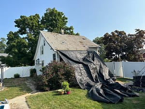 Tarping a residential roof and protecting landscaping prior to old roof removal during a professional roofing project