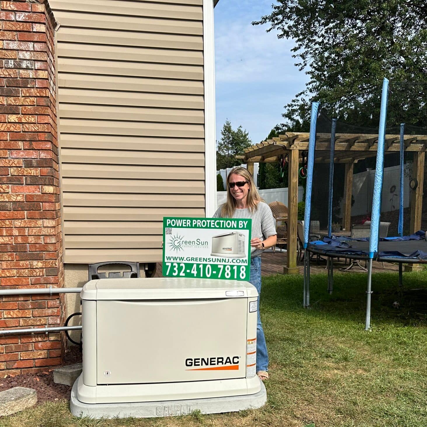 Client holding Green Sun Energy Services, LLC lawn sign near a newly installed Generac home standby generator in Hazlet, NJ.