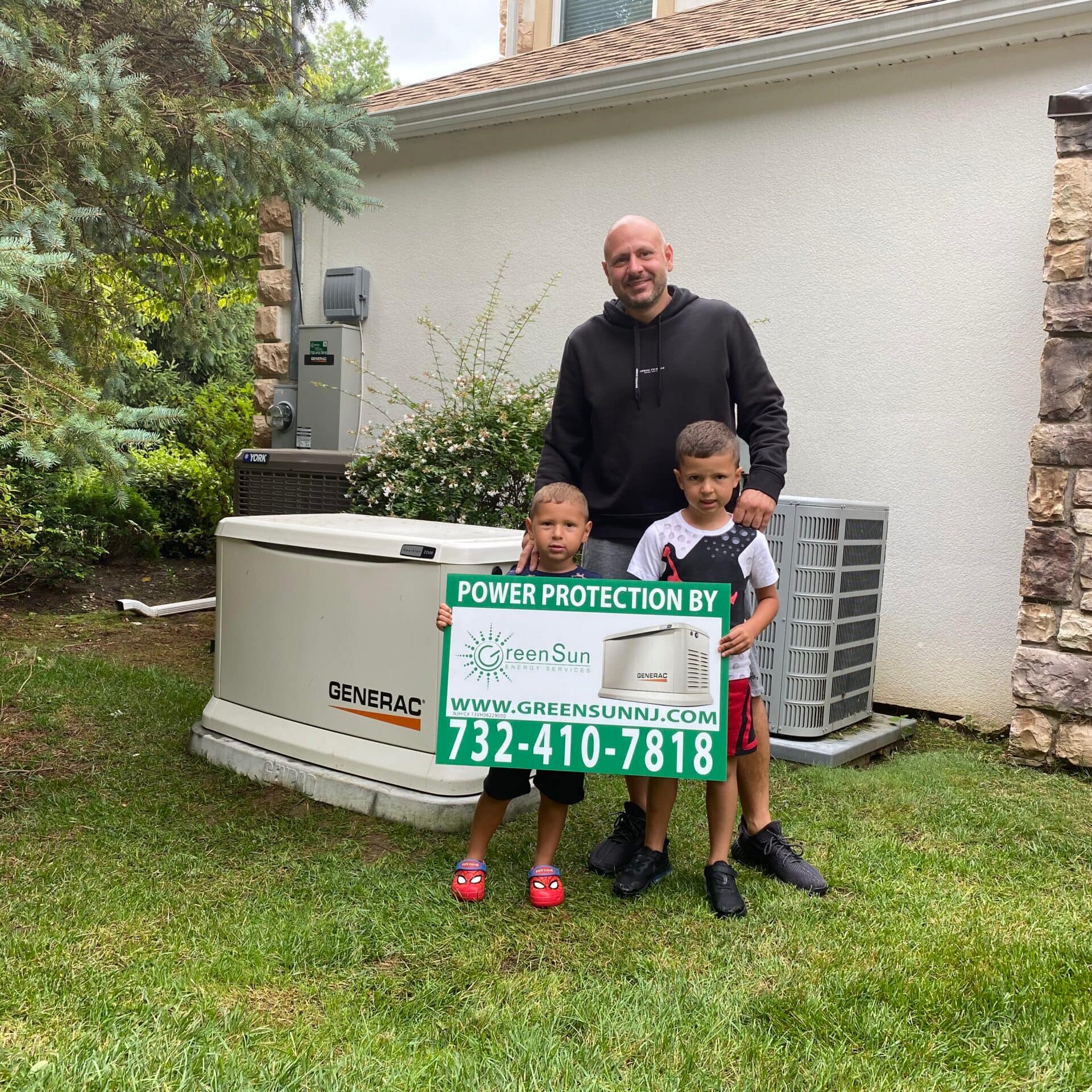 Clients holding Green Sun Energy Services, LLC lawn sign near their newly installed Generac home standby generator in Shrewsbury NJ